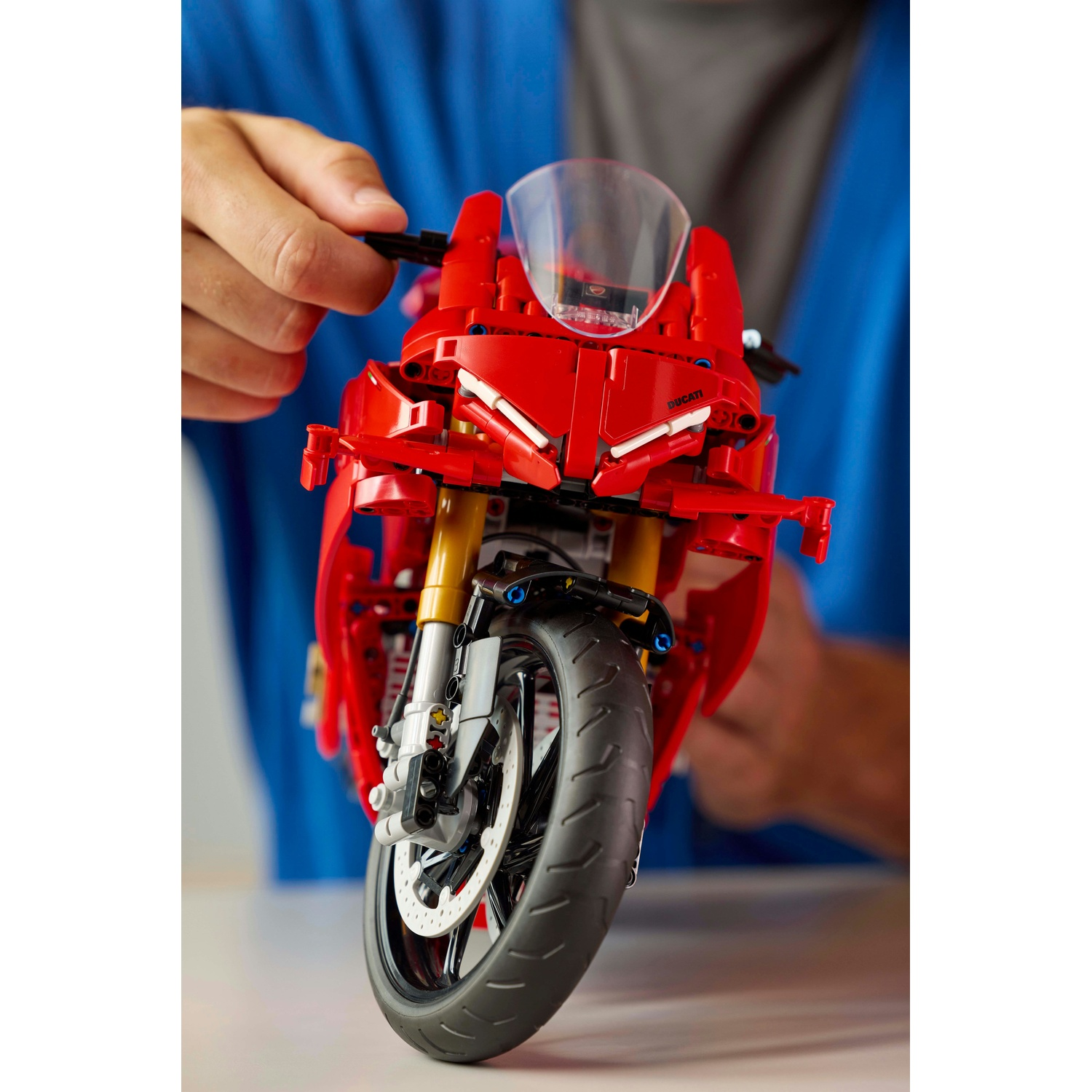 Un giocattolo di moto Ducati rossa è tenuto in mano. La ruota anteriore e la carenatura sono a fuoco. Una mano regola il manubrio.