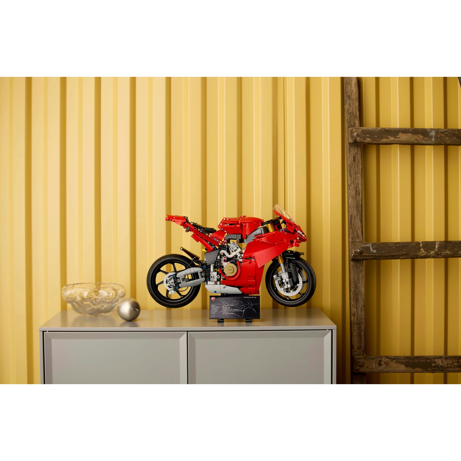 Una moto Ducati Lego rossa su un mobile grigio. Sfondo: parete gialla e scala di legno.