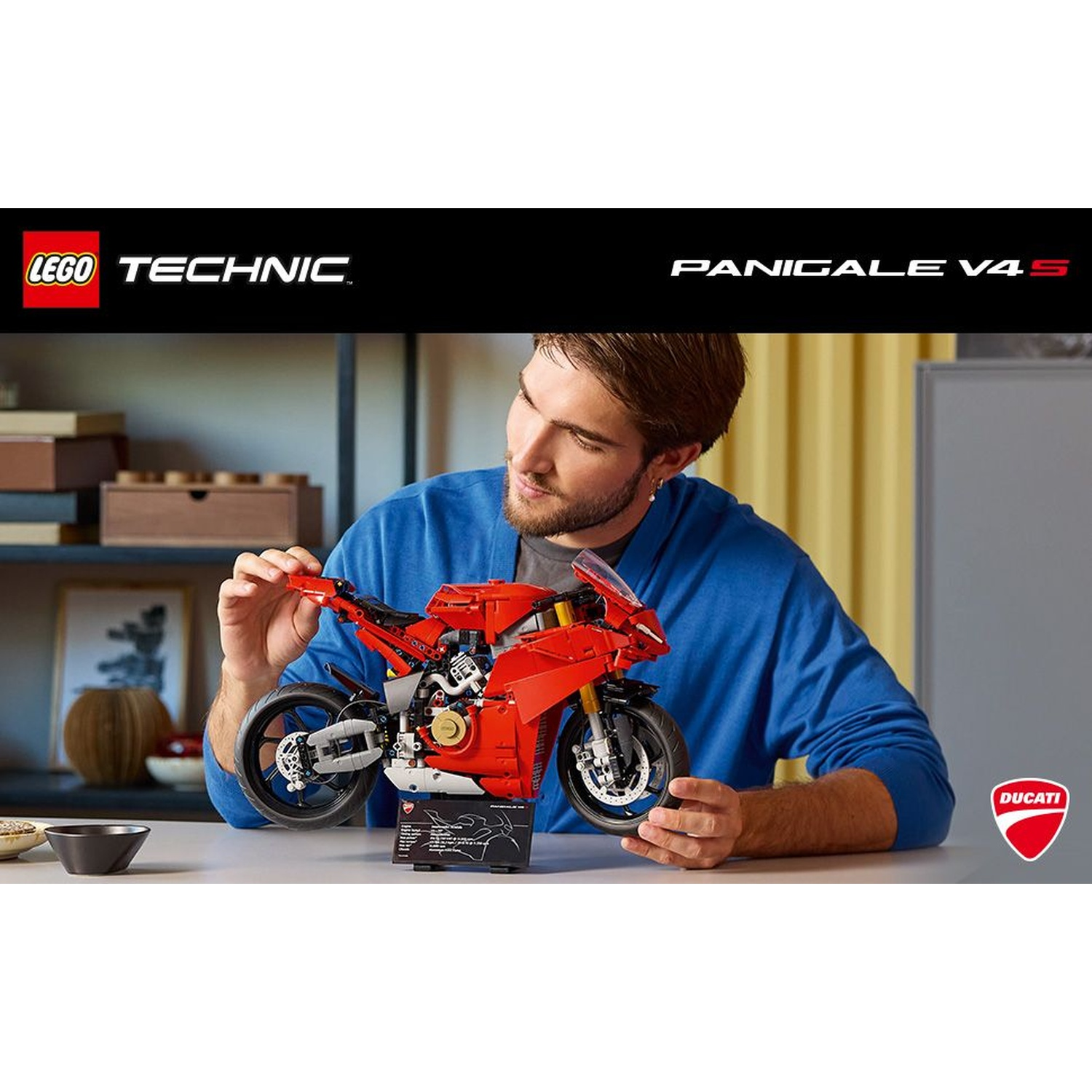 Un uomo assembla un modello di moto Lego Technic Ducati Panigale V4 S rosso. Il modello è su un tavolo. L'uomo indossa una camicia blu.