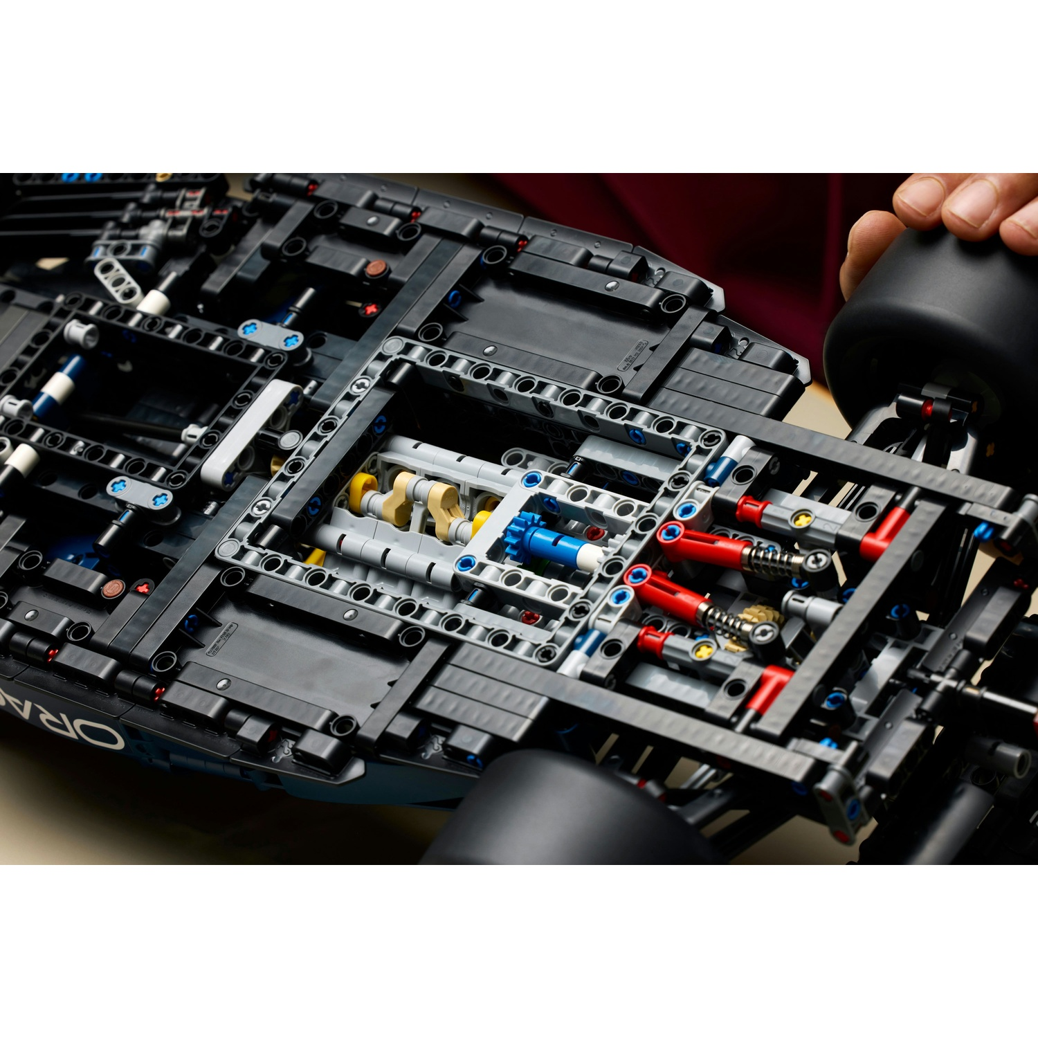 Primo piano del telaio nero di un'auto da corsa Lego. Sono visibili parti del motore. Una mano tiene una gomma nera a destra.