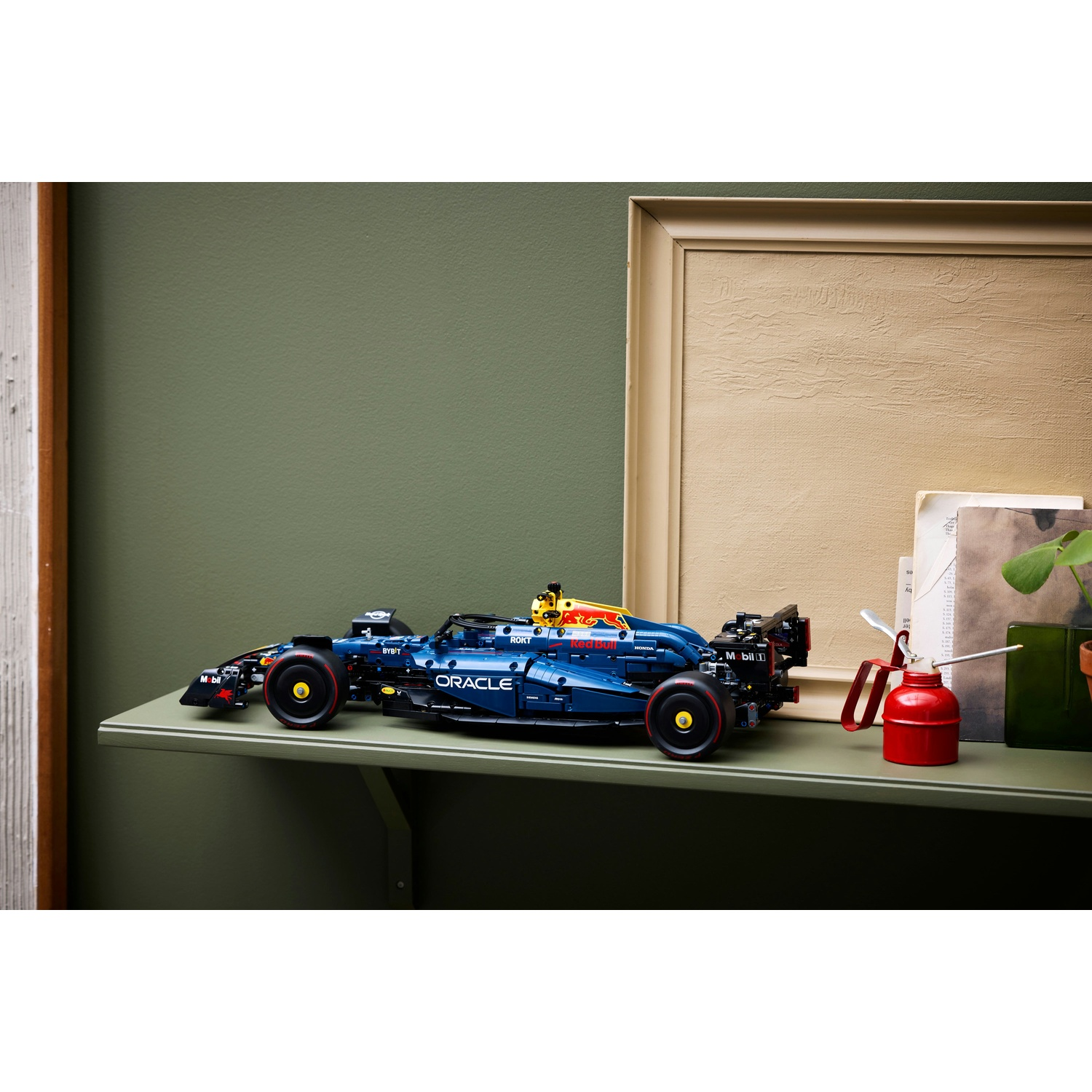 Un modello Lego di auto F1, blu e nero, è su uno scaffale. Un'oliera rossa e una cornice sono dietro. Muro verde.