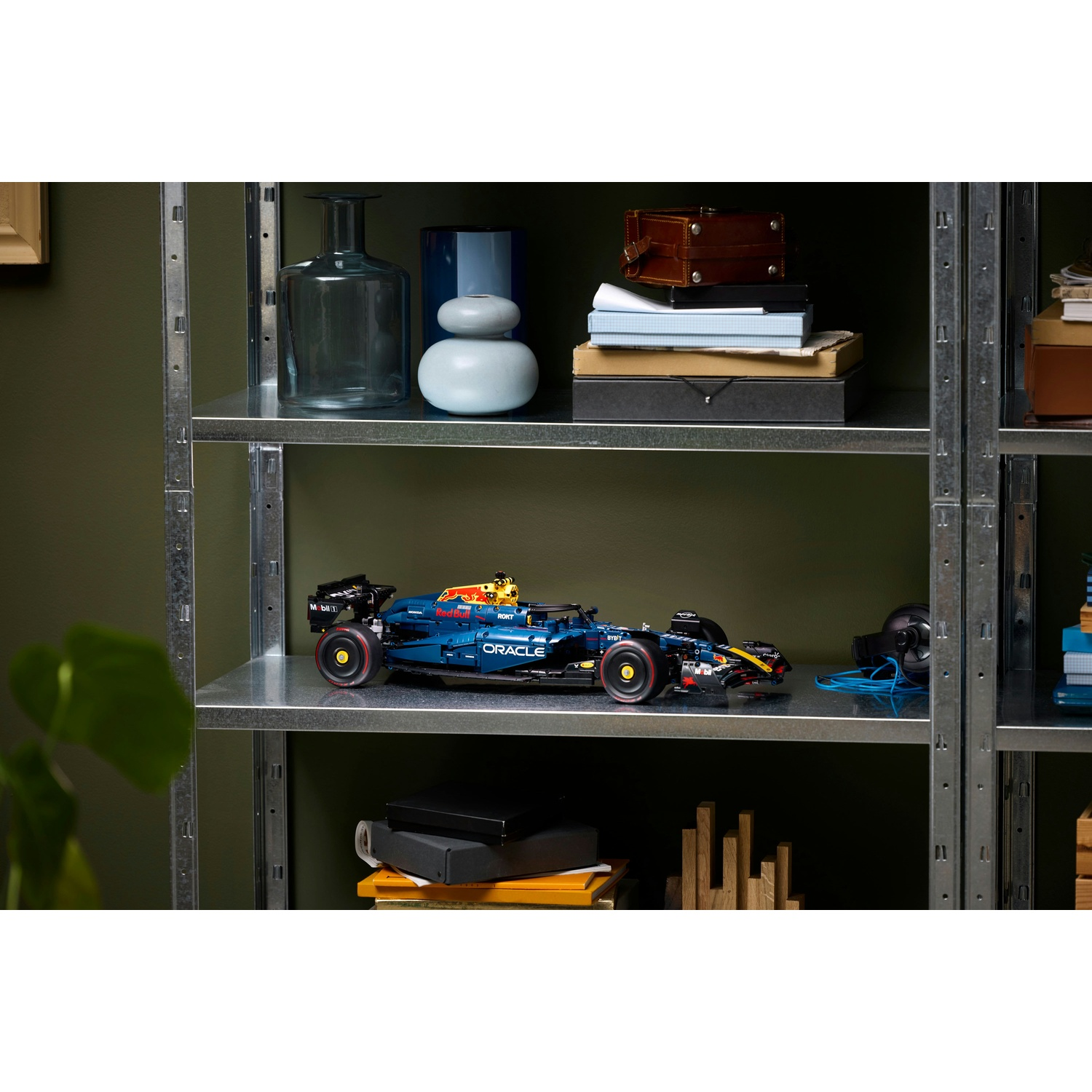 Un'auto di Formula 1 Lego su uno scaffale. Altri oggetti includono vasi, scatole e cuffie. Lo scaffale è in metallo, con sfondo verde.