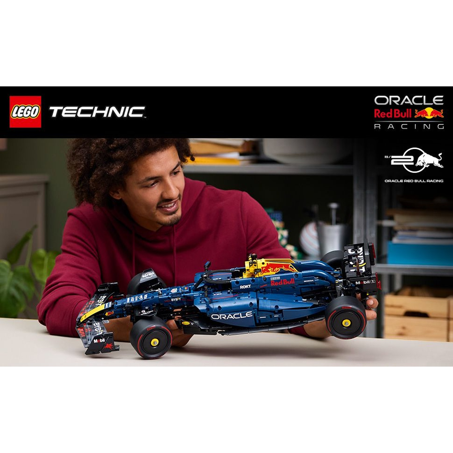 Un uomo tiene una macchina da corsa LEGO Technic Red Bull. L'auto è blu con accenti rossi. I loghi LEGO e Oracle sono visibili.