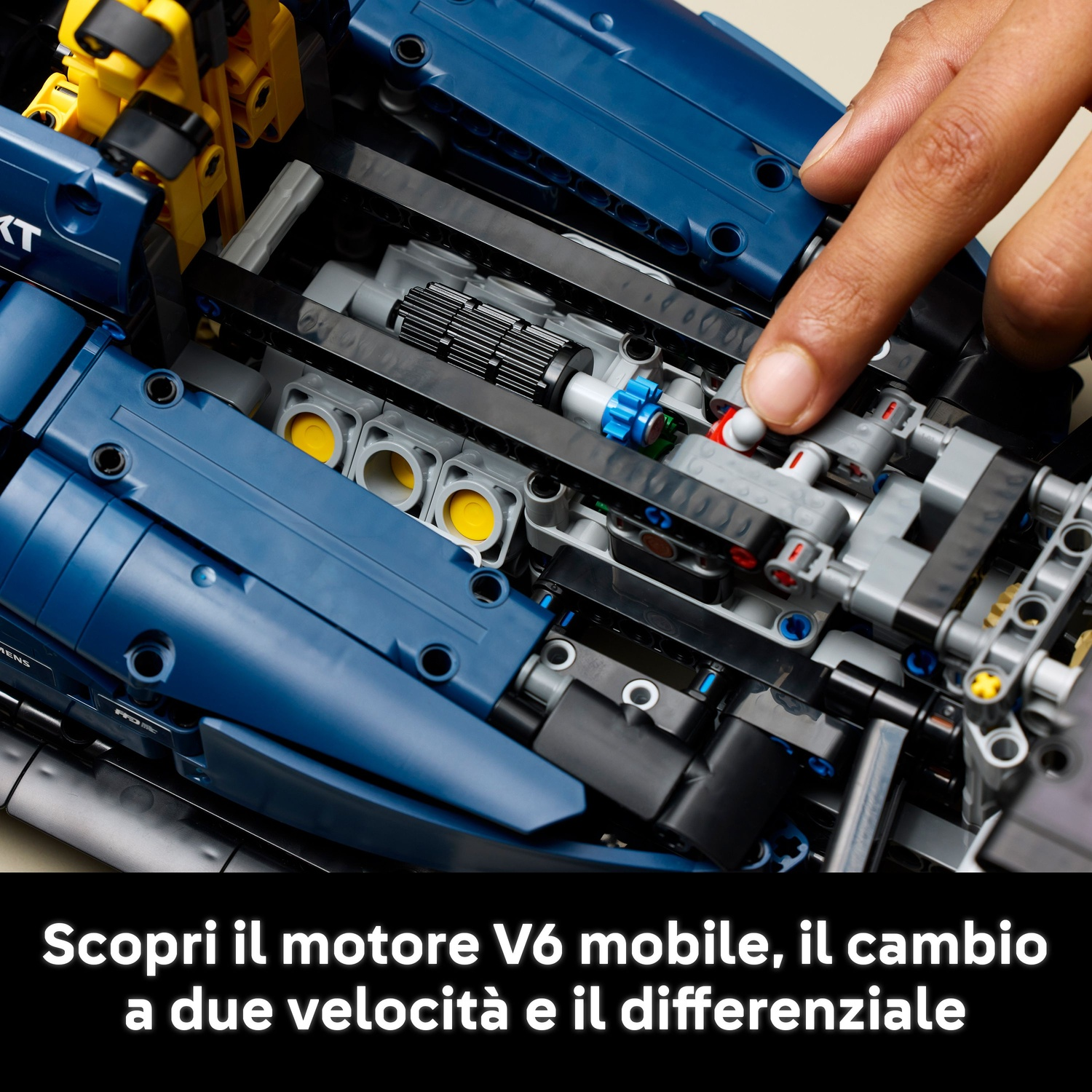 Una mano indica un motore di un'auto Lego blu e nera. Sono visibili parti gialle e grigie. Testo: Scopri il motore V6.