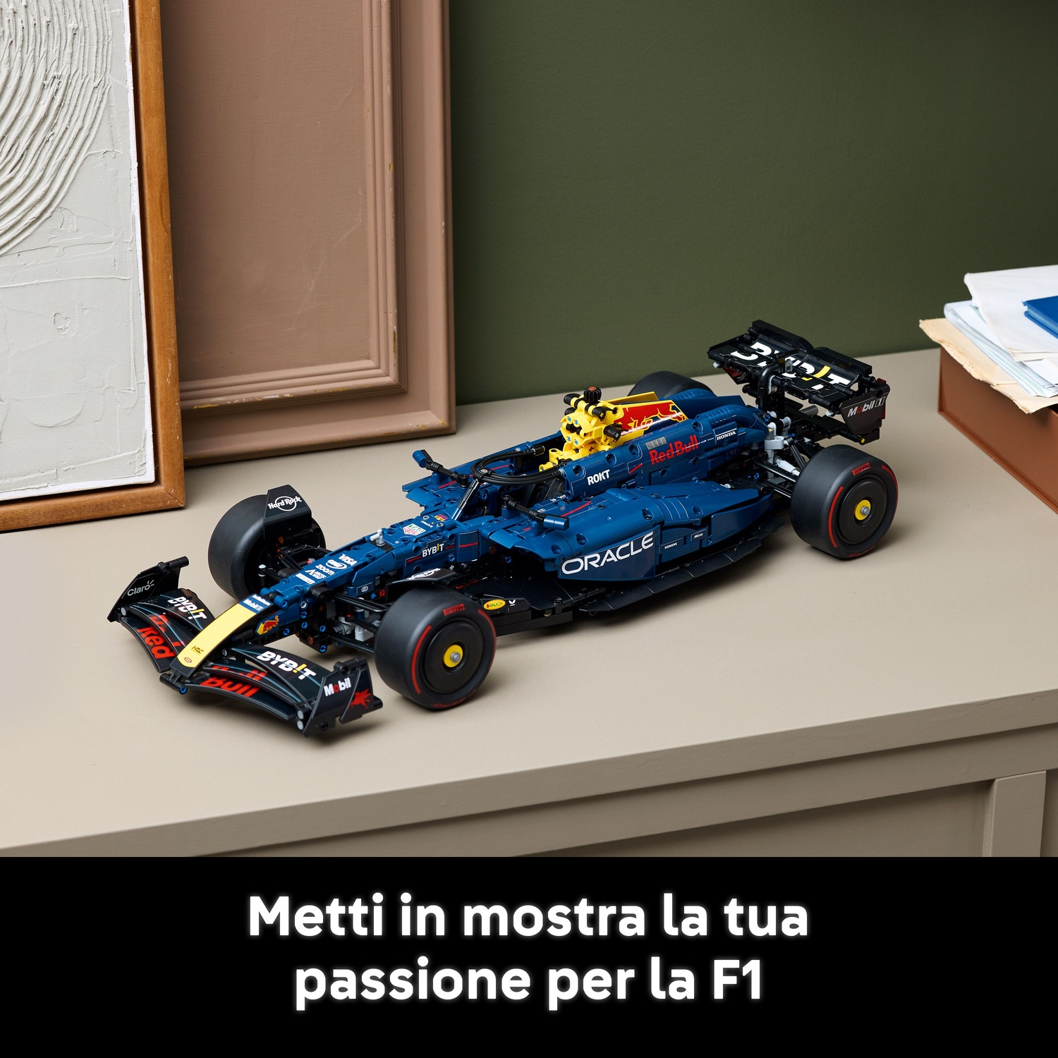 Un'auto modello F1 Red Bull blu scuro su una superficie beige. Cornici e documenti sullo sfondo. L'auto ha i loghi degli sponsor.