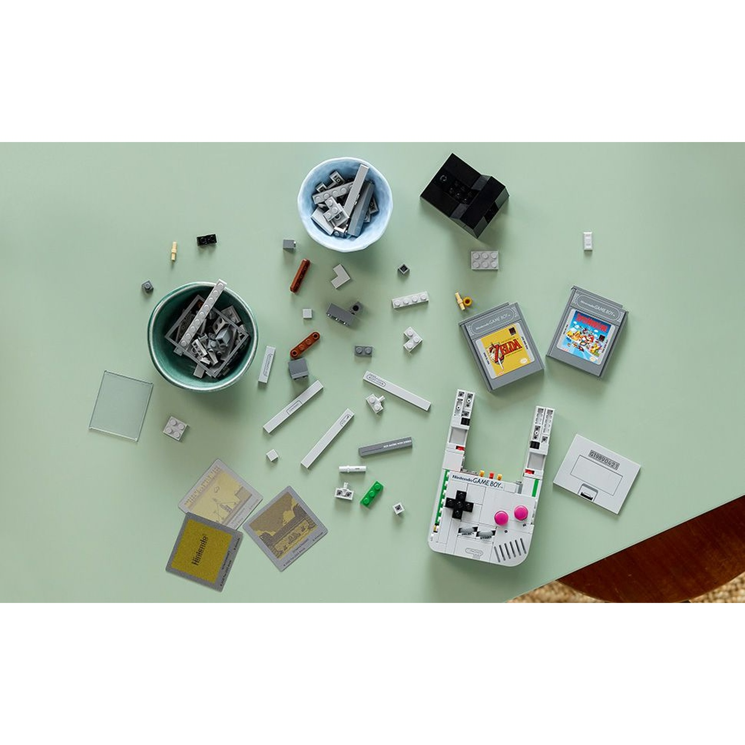 Vista dall'alto di un set Lego Game Boy. Include cartucce di gioco, carte di gioco e vari mattoncini Lego sparsi su una superficie verde.