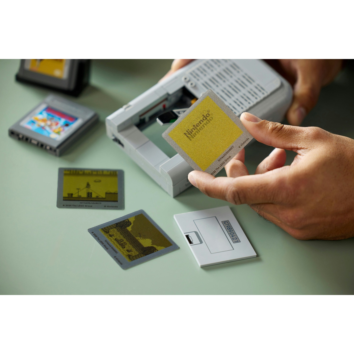 Mani che tengono una carta Nintendo gialla. Altre carte di gioco e una console sono su una superficie verde chiaro.