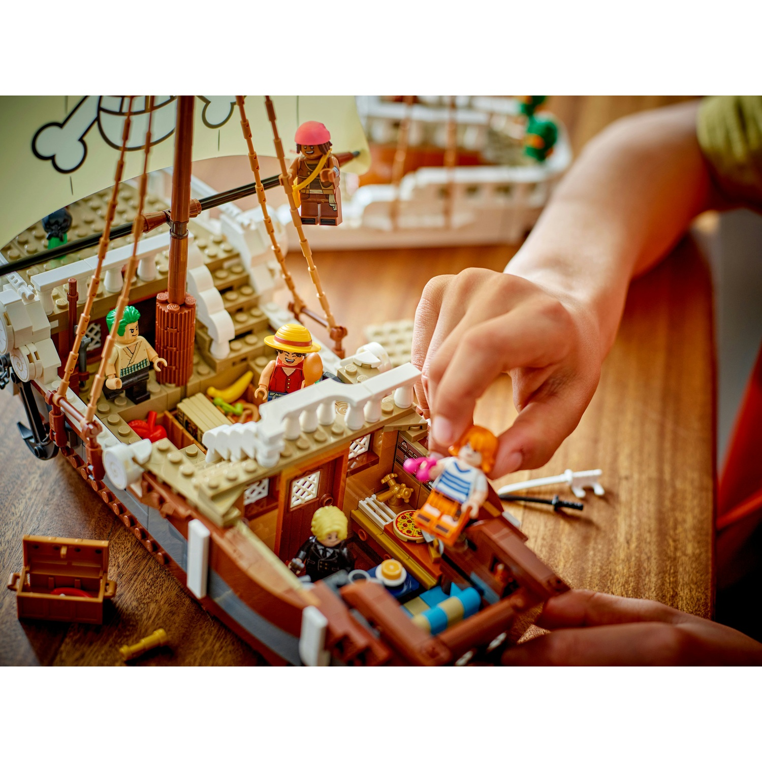Le mani di un bambino che gioca con una nave pirata Lego, con più personaggi Lego e uno scrigno del tesoro su un tavolo di legno.