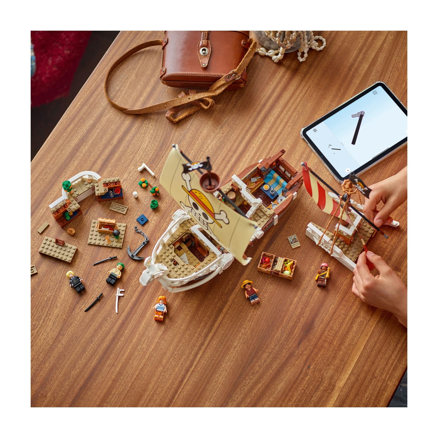 Parti e personaggi di navi Lego sono disposti su un tavolo di legno. Un tablet mostra le istruzioni. Sul tavolo ci sono anche una borsa marrone e dei gioielli.