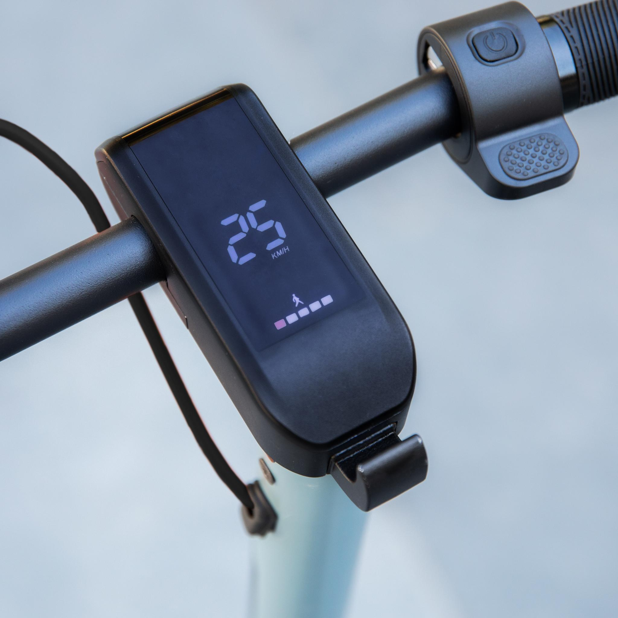 Primer plano del manillar de un patinete eléctrico. La pantalla muestra 25 km/h. Botón de encendido y agarres texturizados.