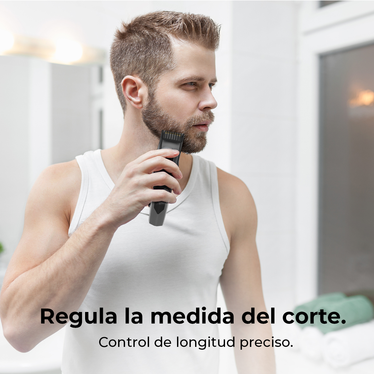 Un hombre se afeita la barba con una recortadora eléctrica en un baño. Lleva una camiseta sin mangas blanca y mira hacia un lado.