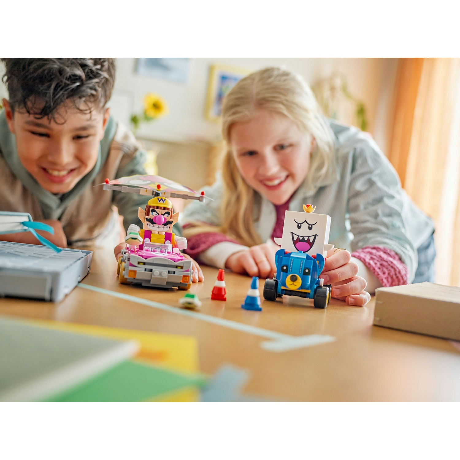 Due bambini sorridono, giocando con set Lego Mario Kart. Uno presenta Wario, l'altro un personaggio simile a Boo. Accessori sul tavolo.