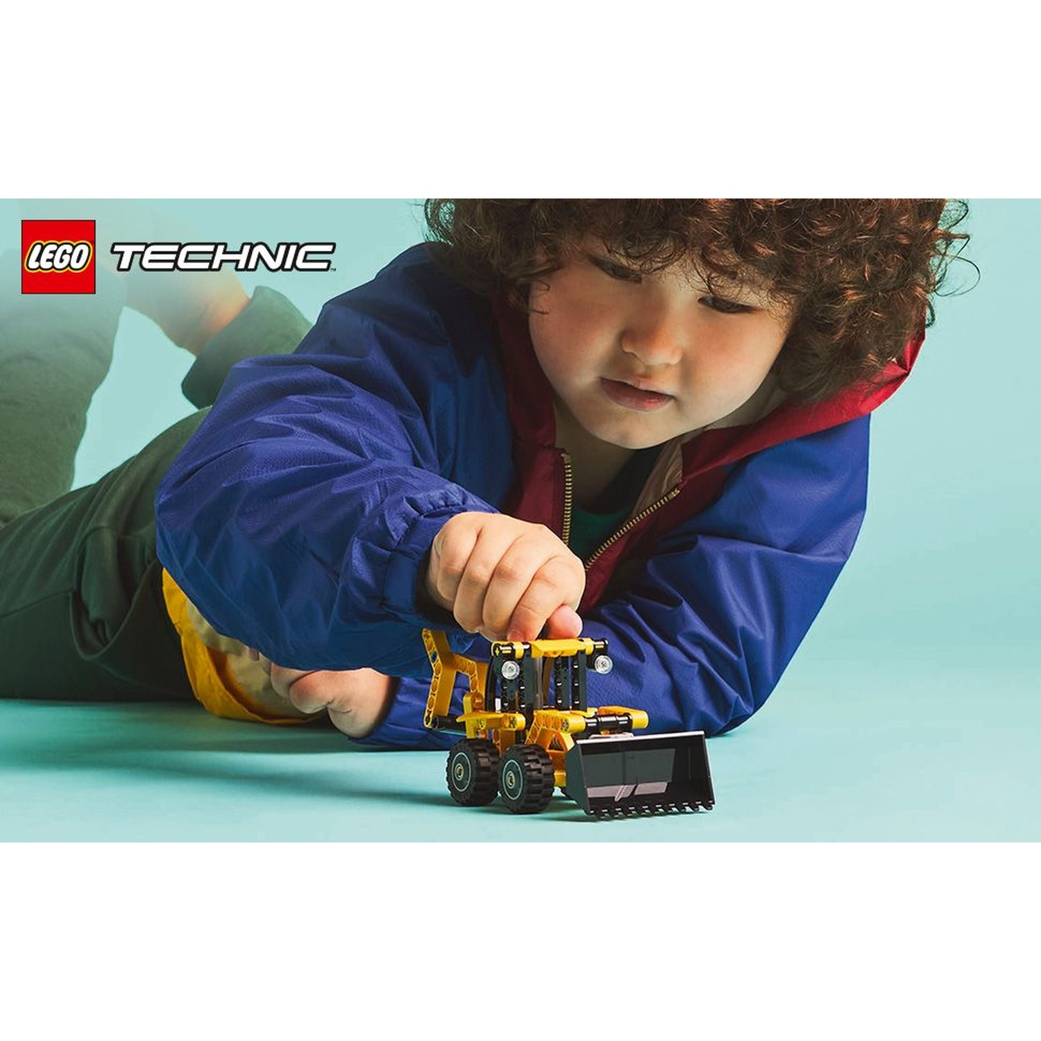 Un bambino gioca con un bulldozer giocattolo Lego Technic giallo e nero. Il bambino indossa una giacca blu.