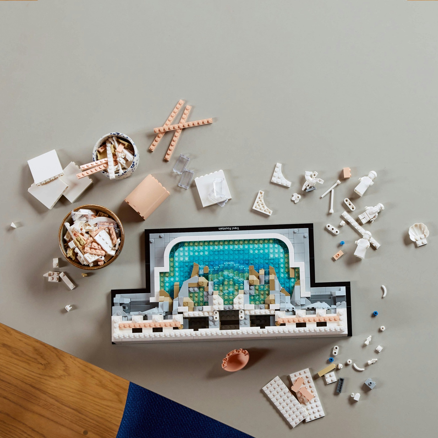 Un set Lego della Fontana di Trevi è circondato da pezzi sparsi. Ci sono ciotole di mattoncini e sezioni della costruzione su una superficie grigia.