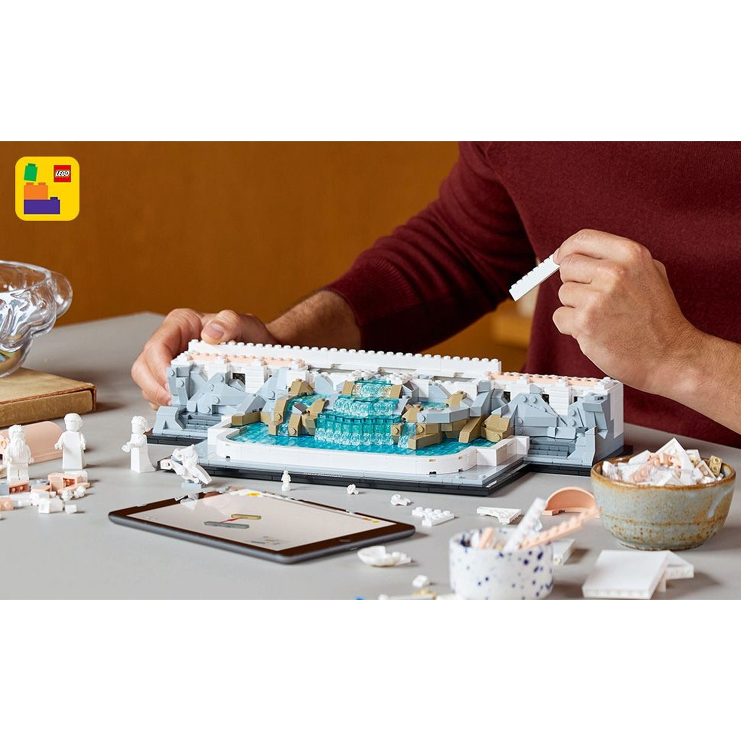 Una persona costruisce un modello Lego di una fontana. Parti, un tablet e ciotole con pezzi sono sul tavolo.
