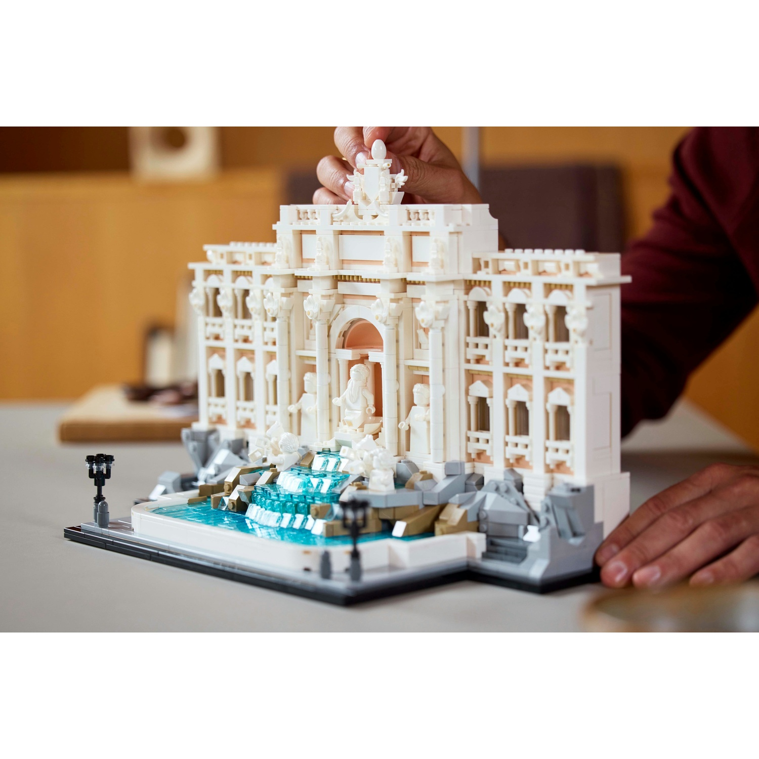 Un modello Lego della Fontana di Trevi bianca con acqua blu. Una mano sta mettendo un pezzo sopra.