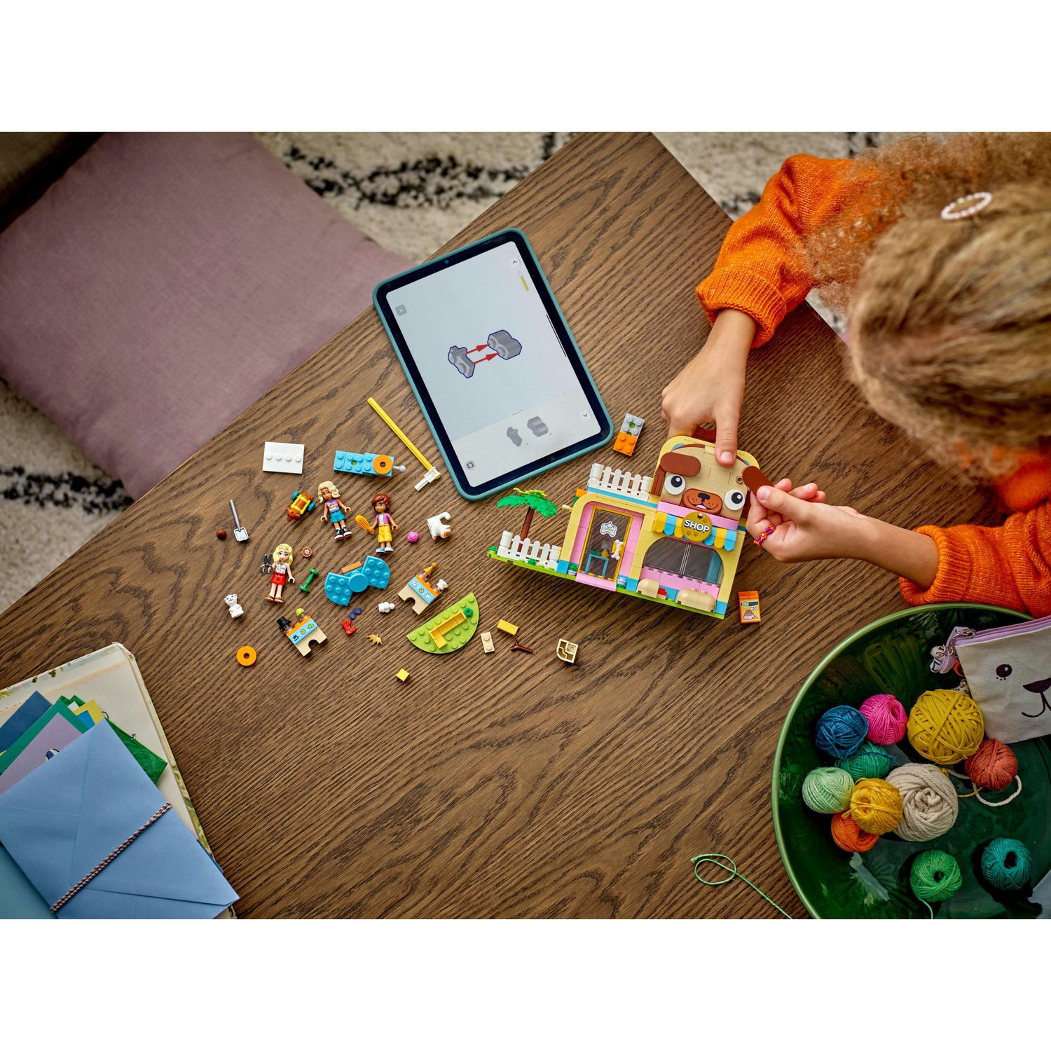 Un bambino assembla un set Lego su un tavolo di legno. Il set include un negozio a tema cane. Sono presenti vari pezzi Lego e un iPad.