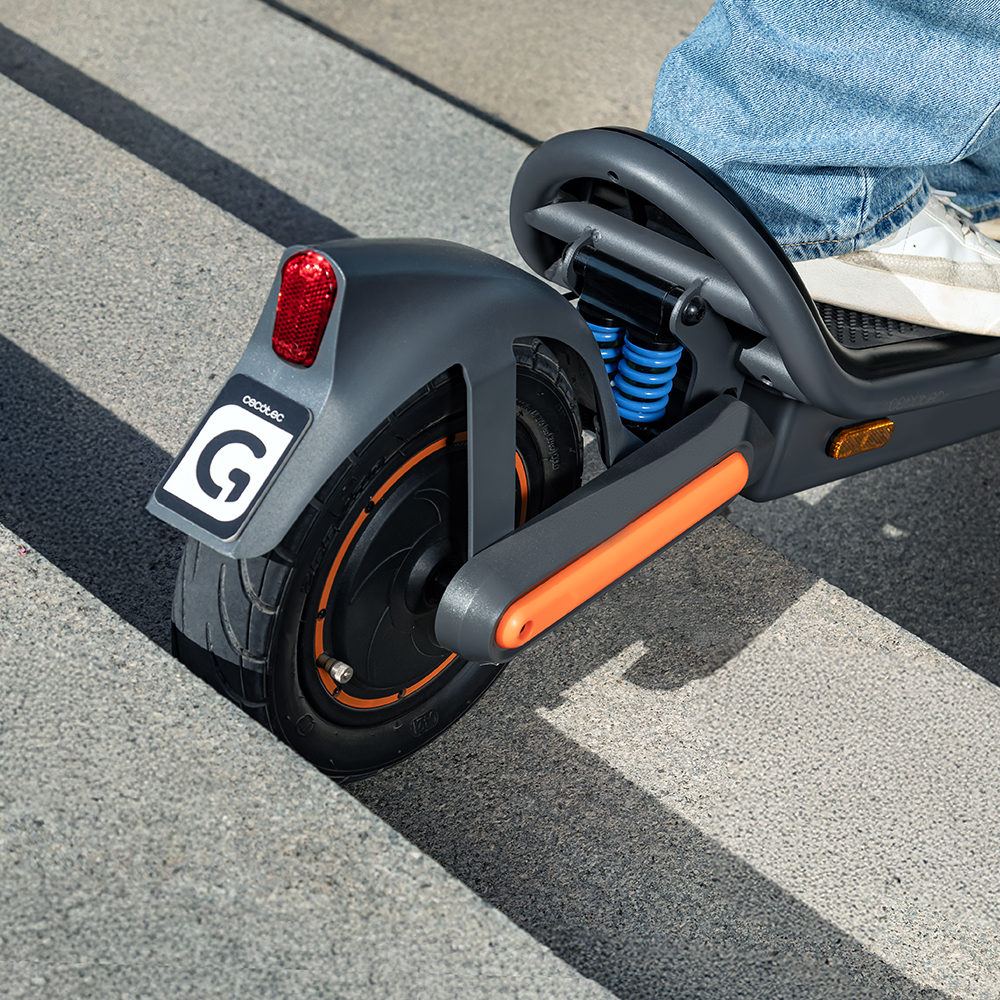 Primer plano de un patinete eléctrico. Se ve la rueda trasera, guardabarros gris con luz roja y matrícula, detalles naranjas.
