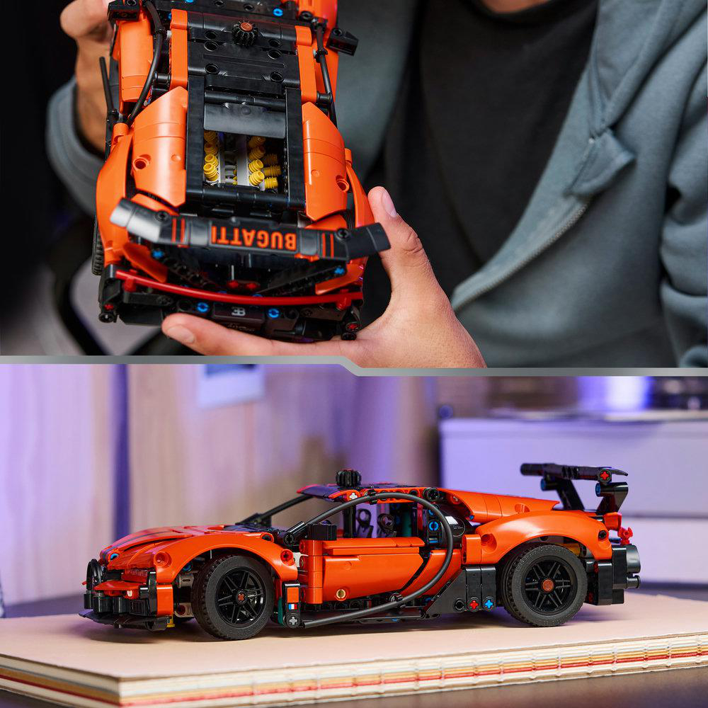 Ein orangefarbenes Bugatti Lego-Auto wird von einer Person gehalten. Ein weiteres, montiertes Auto steht auf einer Oberfläche. Das Auto hat schwarze Räder und einen Spoiler.