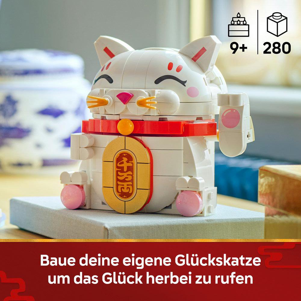 Eine weiße Glückskatze aus Blöcken, mit rotem Halsband und goldenem Anhänger, auf grauem Sockel. 9+ und 280 sind angegeben.