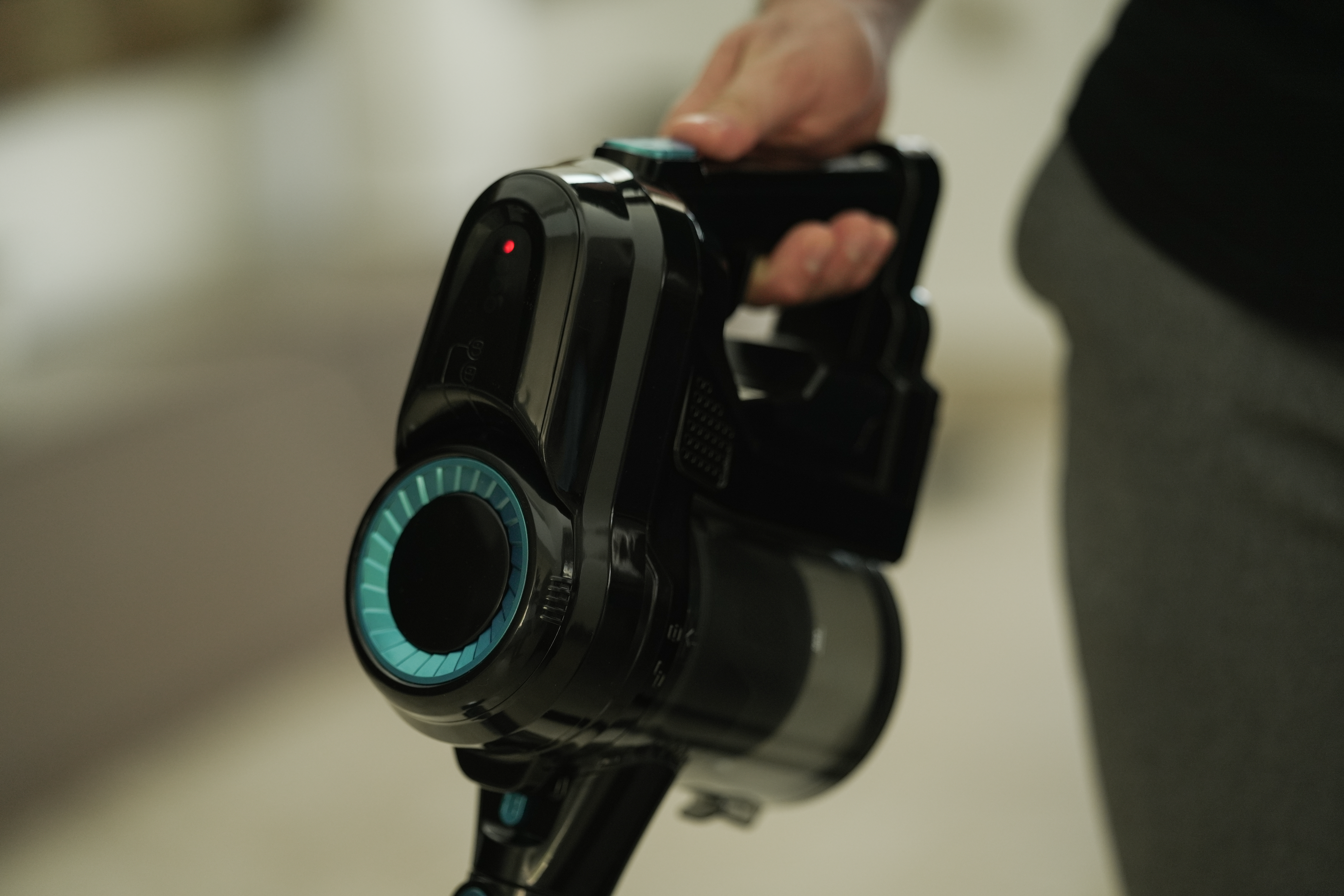 Czarno-niebieski odkurzacz ręczny jest trzymany przez osobę. Świeci się czerwone światło.