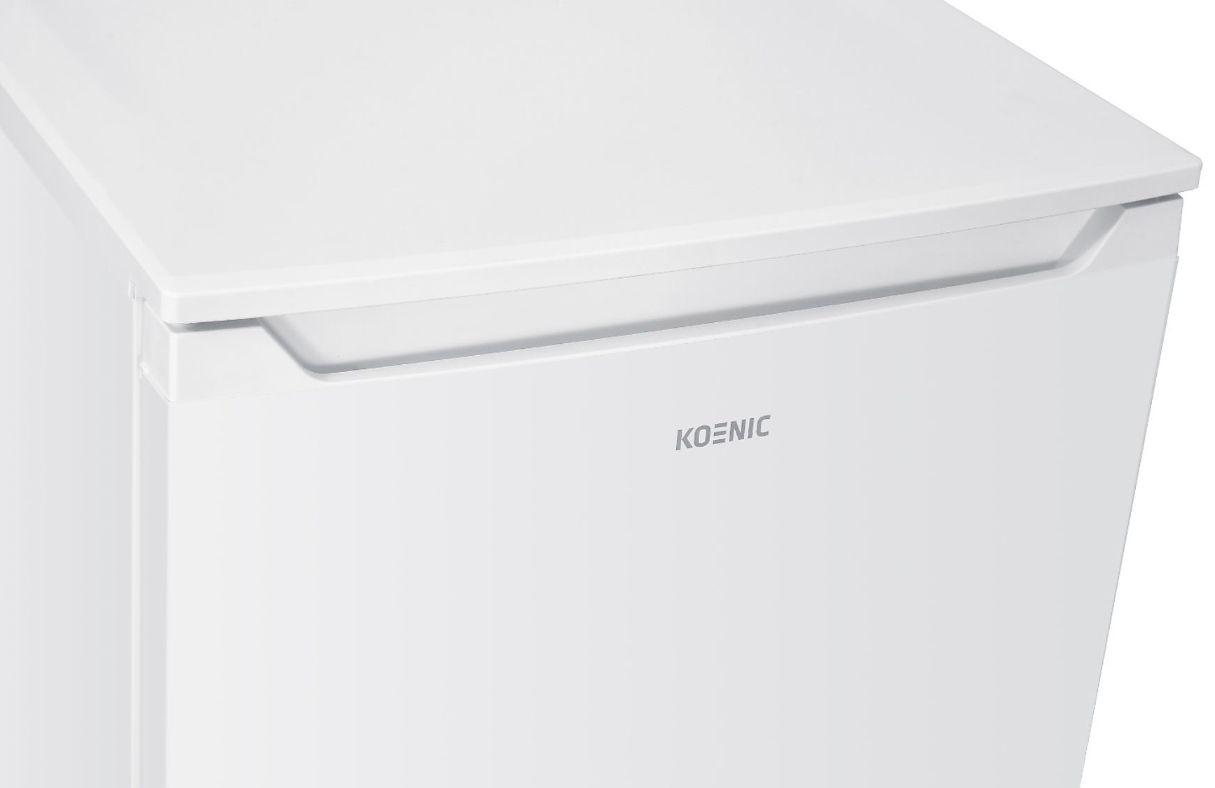 Zbliżenie białej lodówki z marką 'KOENIC'. Góra jest lekko pochylona. Drzwi mają uchwyt.