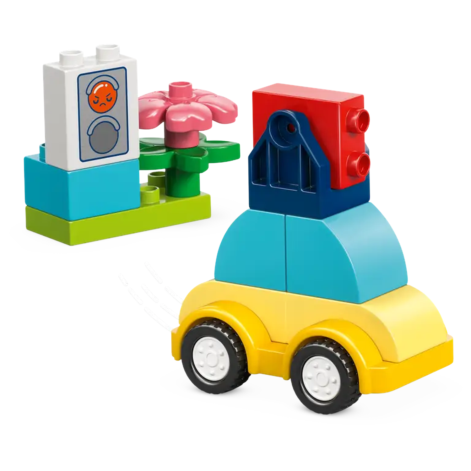 A toy car made of blocks and a flower are on a white surface. The car is yellow with blue and red blocks. The flower is pink.