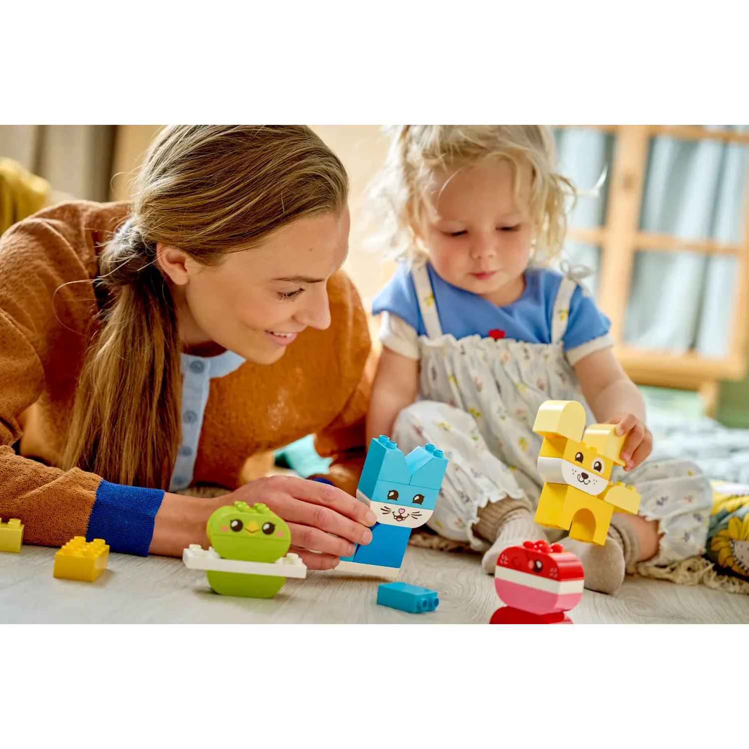 A woman and a child are playing with Lego. There are animal-shaped blocks in different colors on the floor.