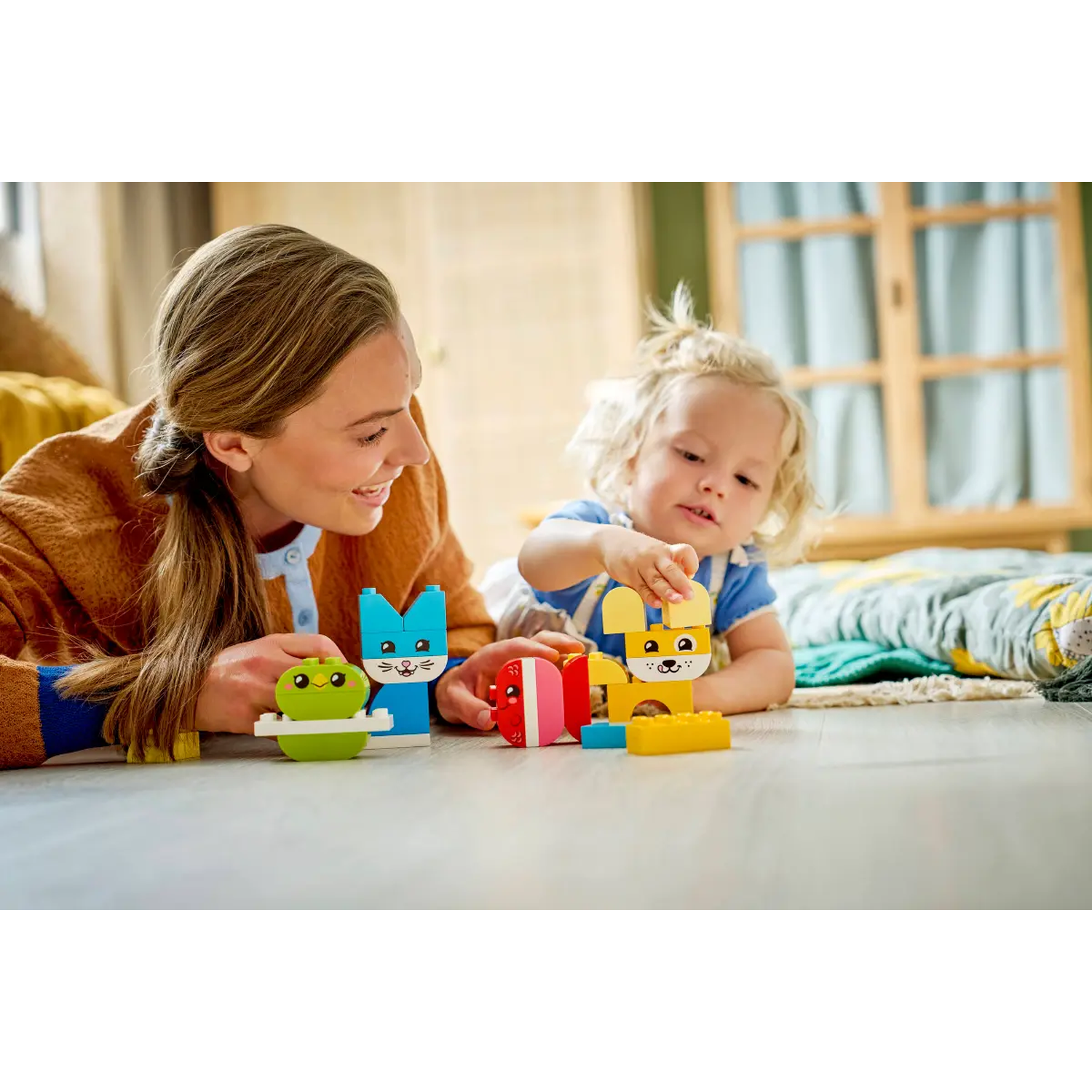 A woman and a child are playing with colorful toy blocks on the floor. The child is reaching for a yellow rabbit.