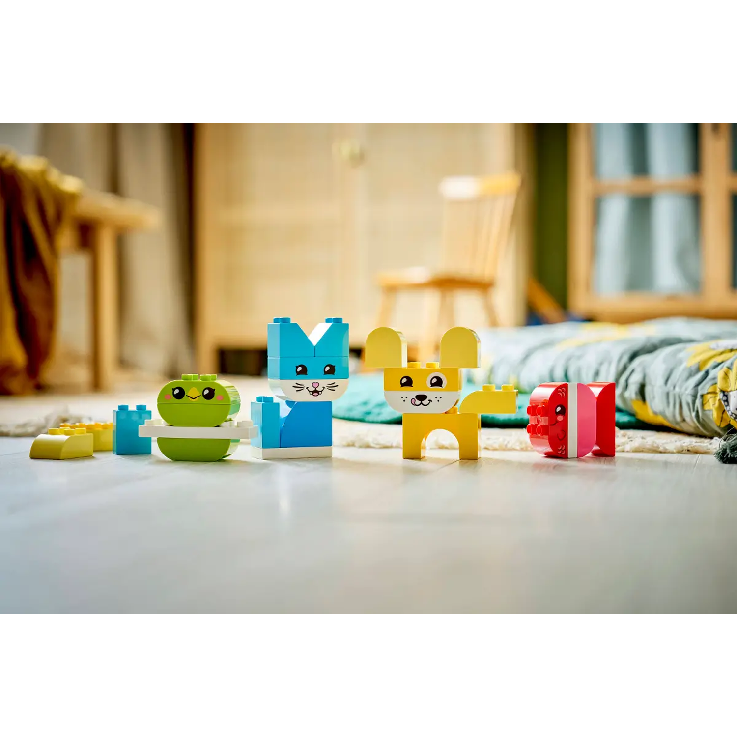 Colorful Lego animal toys: a green frog, blue cat, yellow dog, and red gift. They are on a light floor, with blurred background.