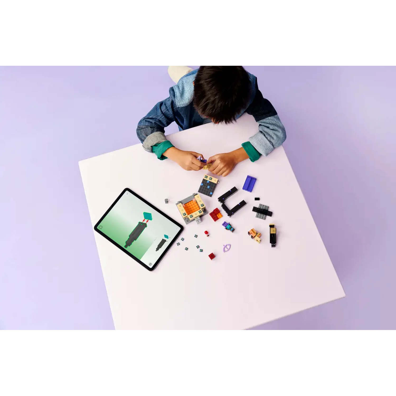 A child is building with Lego bricks on a white table, using a tablet. Various colored bricks and a partially built structure are present.