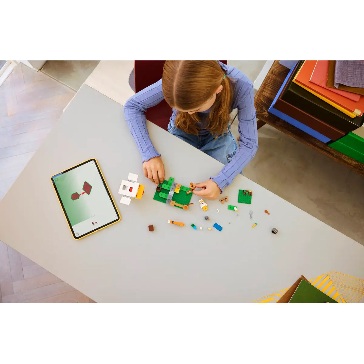 Een meisje bouwt een Lego-set op tafel. Een tablet toont instructies. Diverse Lego-onderdelen liggen verspreid.