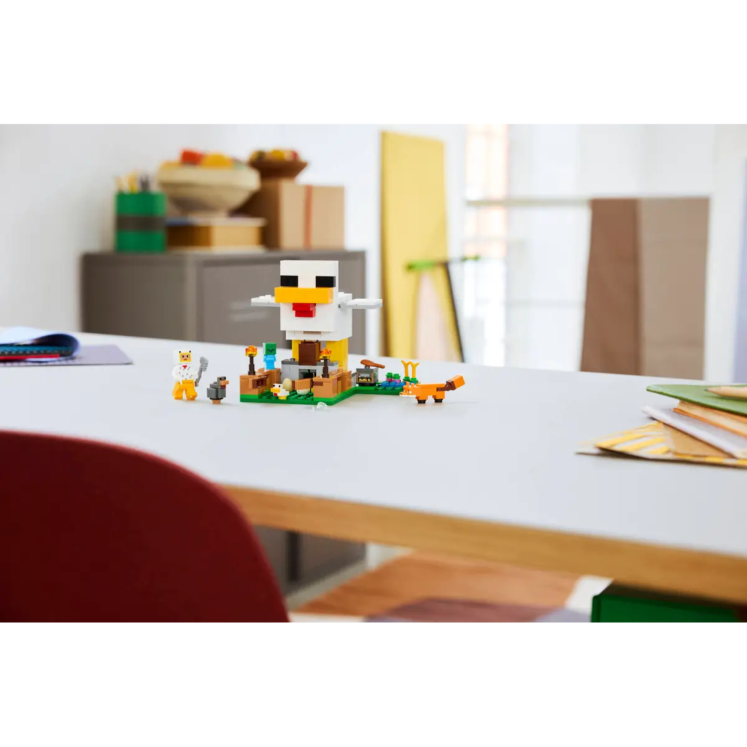 Een Minecraft Lego set op een witte tafel. Een grote kippenfiguur staat naast kleinere figuren, waaronder een vos. Achtergrond wazig.