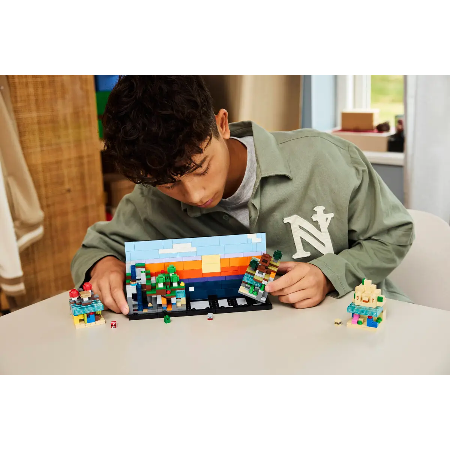A person builds a Lego diorama on a table. The diorama shows a cityscape with colorful blocks. The person is focused on the construction.