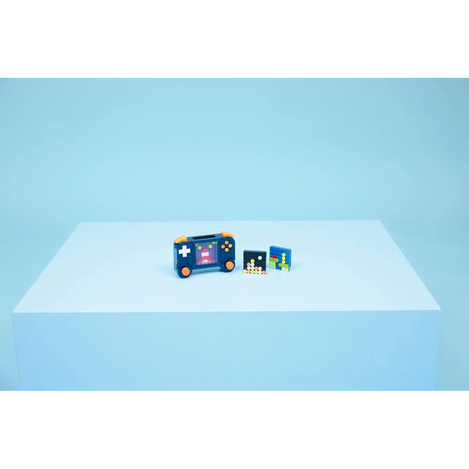 A toy video game and two game cartridges sit on a white surface against a light blue background.