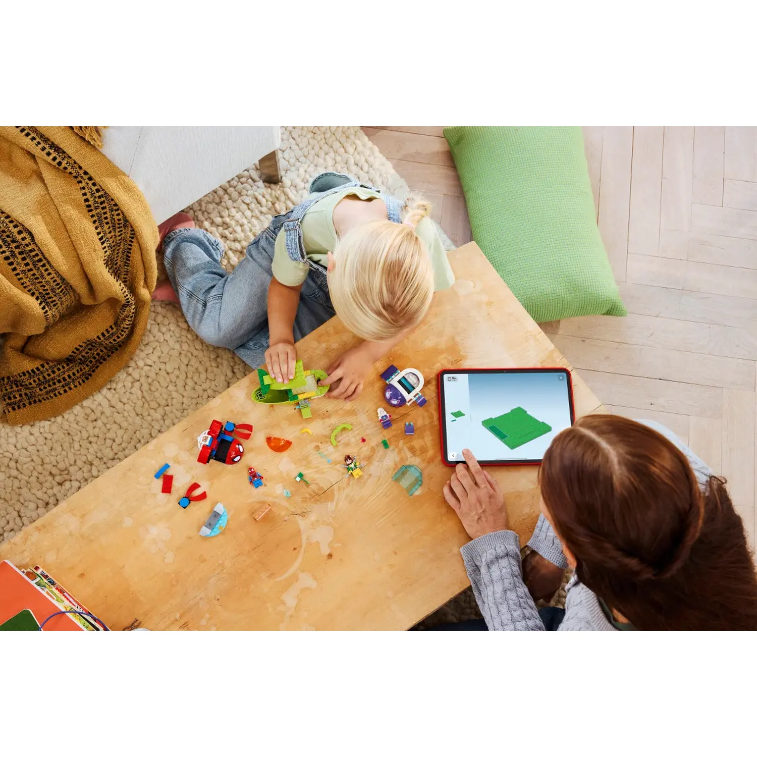 Un enfant et un adulte jouent avec des LEGO sur une table en bois. L'enfant construit un jouet, tandis que l'adulte utilise une tablette.