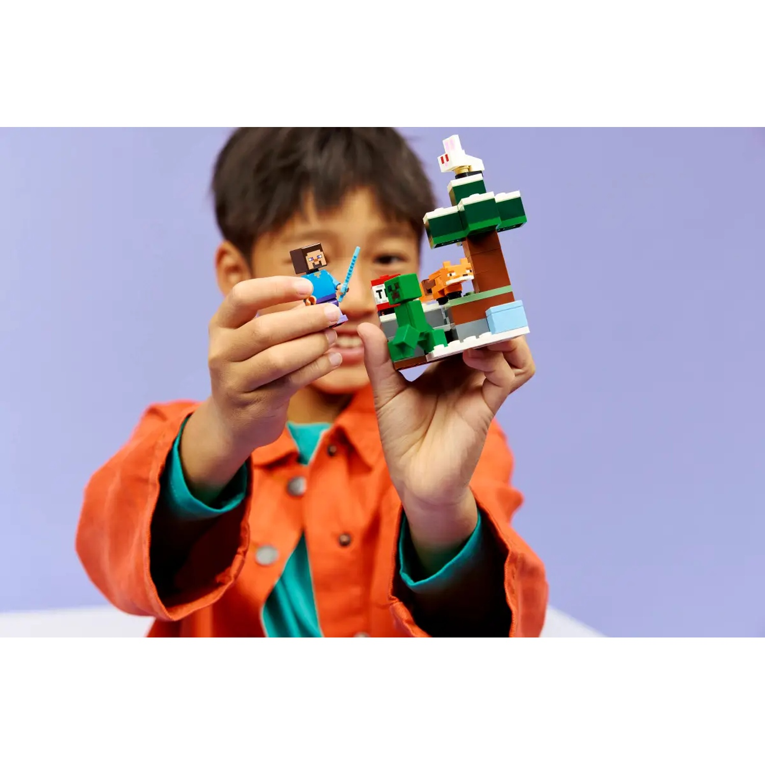 Un enfant tient un set Lego Minecraft. L'ensemble comprend une figurine de Steve, un Creeper, un renard et un arbre sur une base blanche.