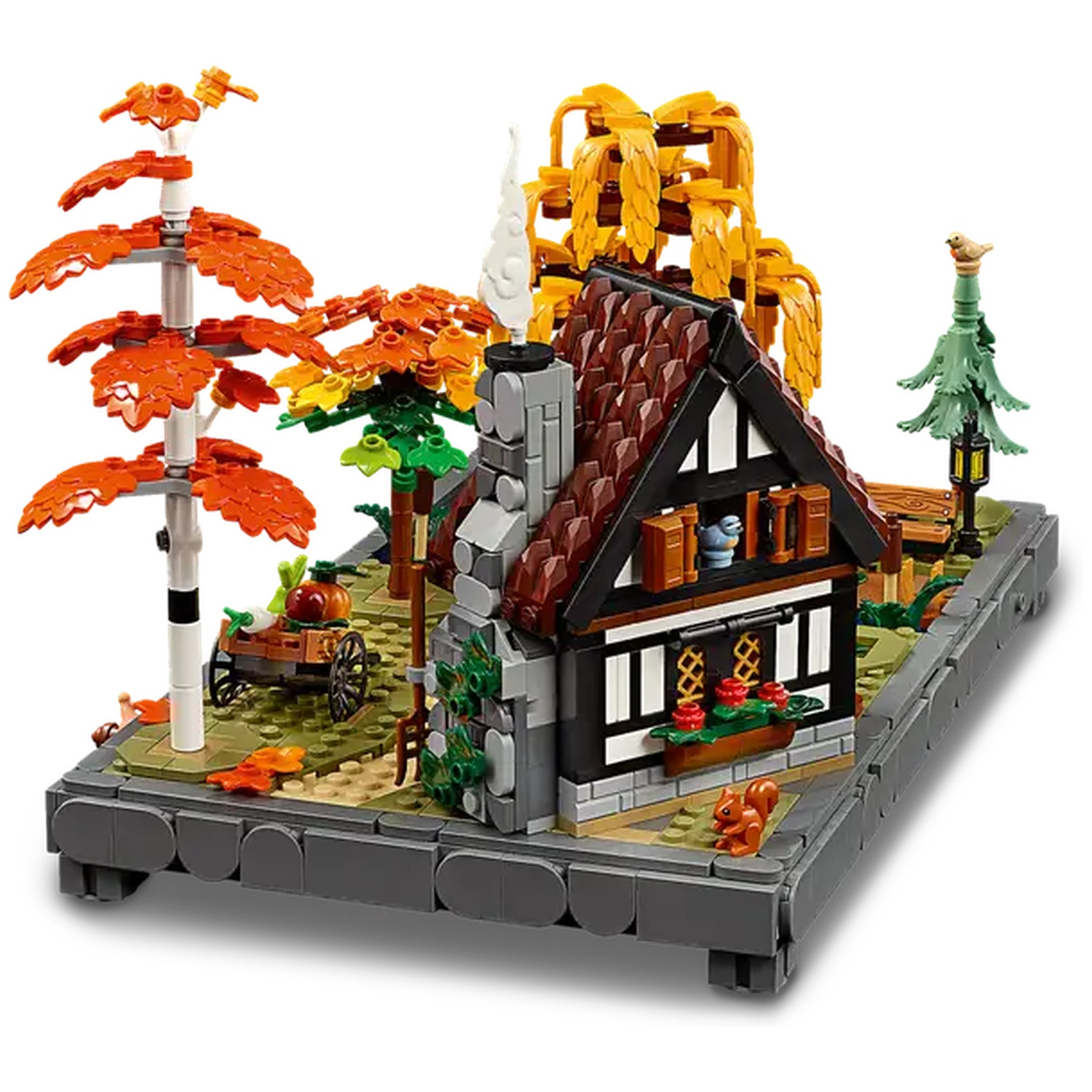 Un modèle Lego d'un cottage avec un toit rouge. Il y a des arbres aux feuilles oranges, une charrette et un écureuil.