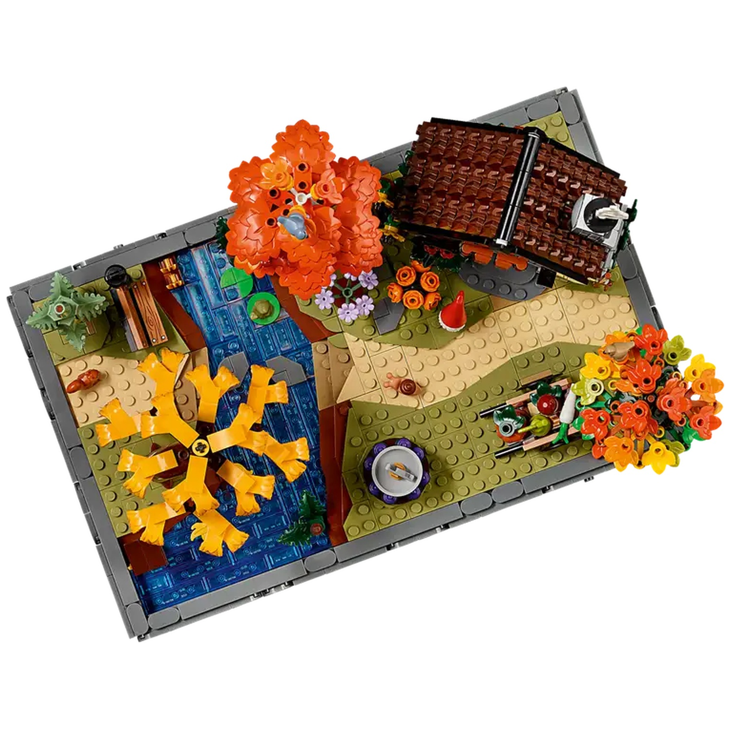 Un diorama Lego présente une petite maison, des arbres, un étang et divers arrangements floraux. La scène se déroule sur une base grise.