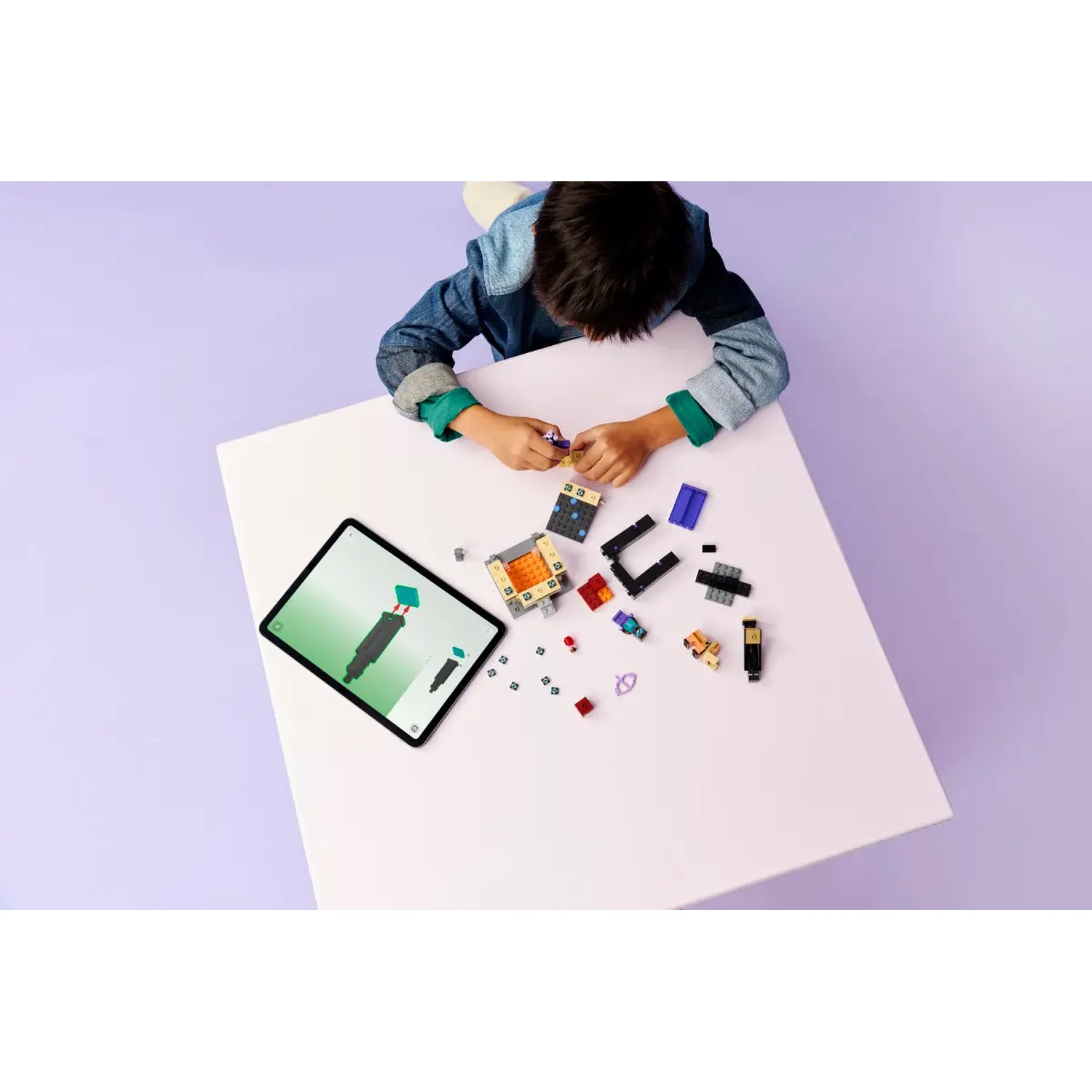 Un enfant construit avec des LEGO sur une table blanche, avec une tablette affichant des instructions. Diverses pièces et ensembles LEGO sont éparpillés.
