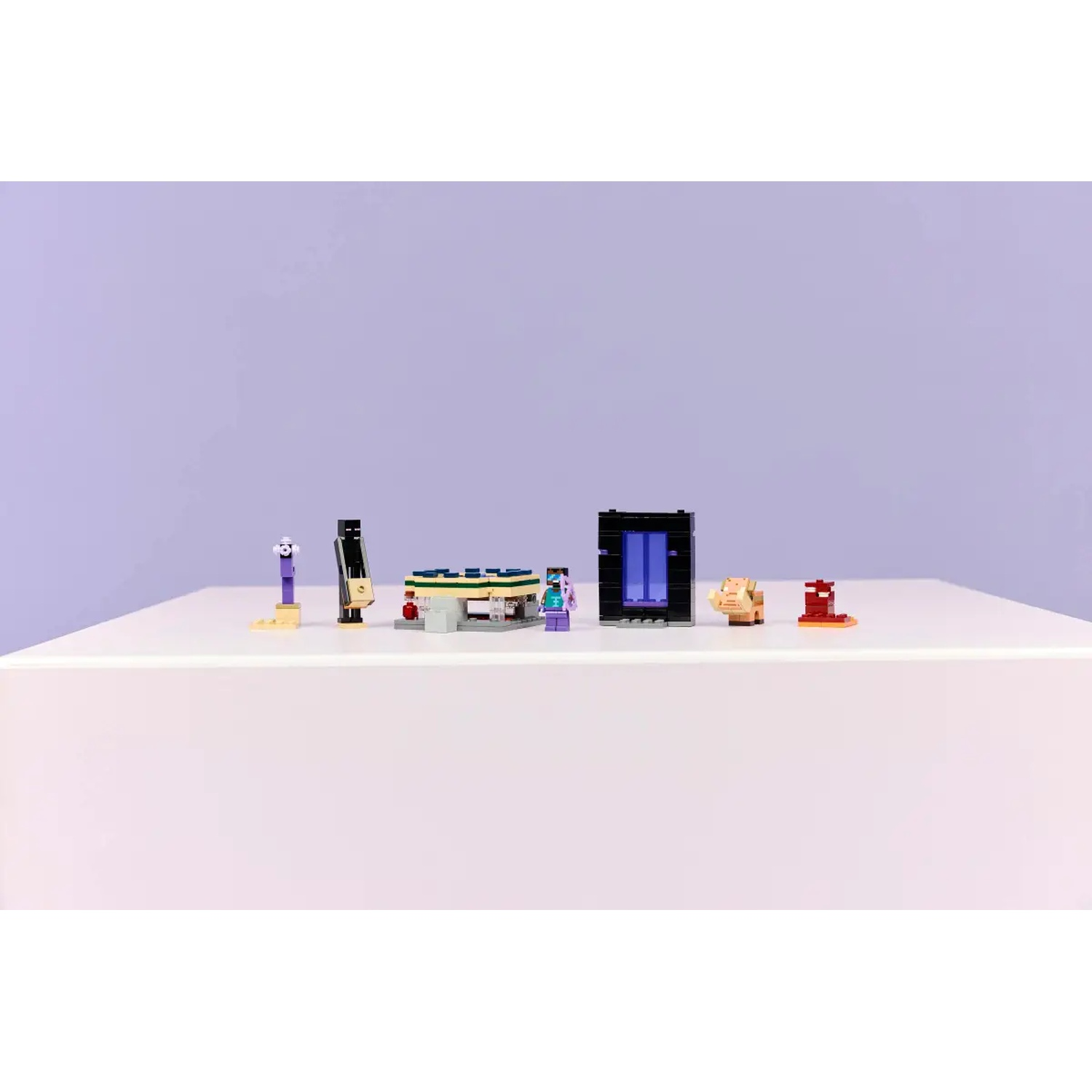 Une table blanche présente divers ensembles Lego Minecraft. Comprend un portail, des figurines et des structures, sur fond violet.