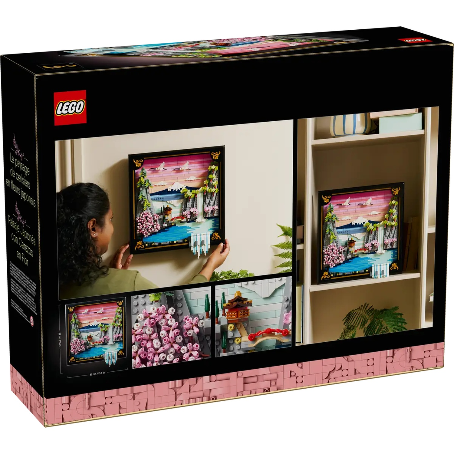 A Lego box shows a woman hanging a Lego art set. The set depicts a Japanese landscape with cherry blossoms, water, and mountains.