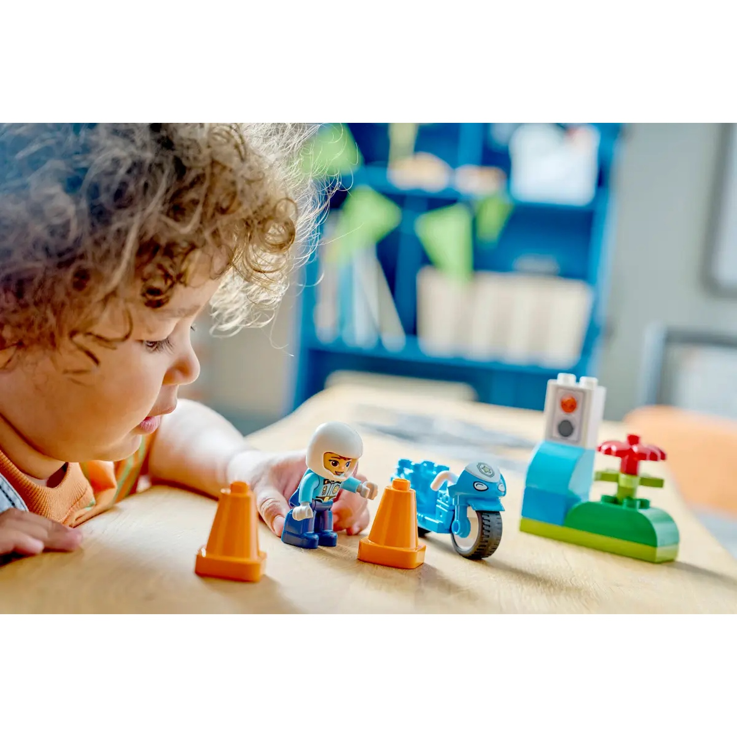 Un enfant joue avec des jouets Lego Duplo. Comprend une moto bleue, une figurine de policier, des cônes oranges et un feu tricolore vert.