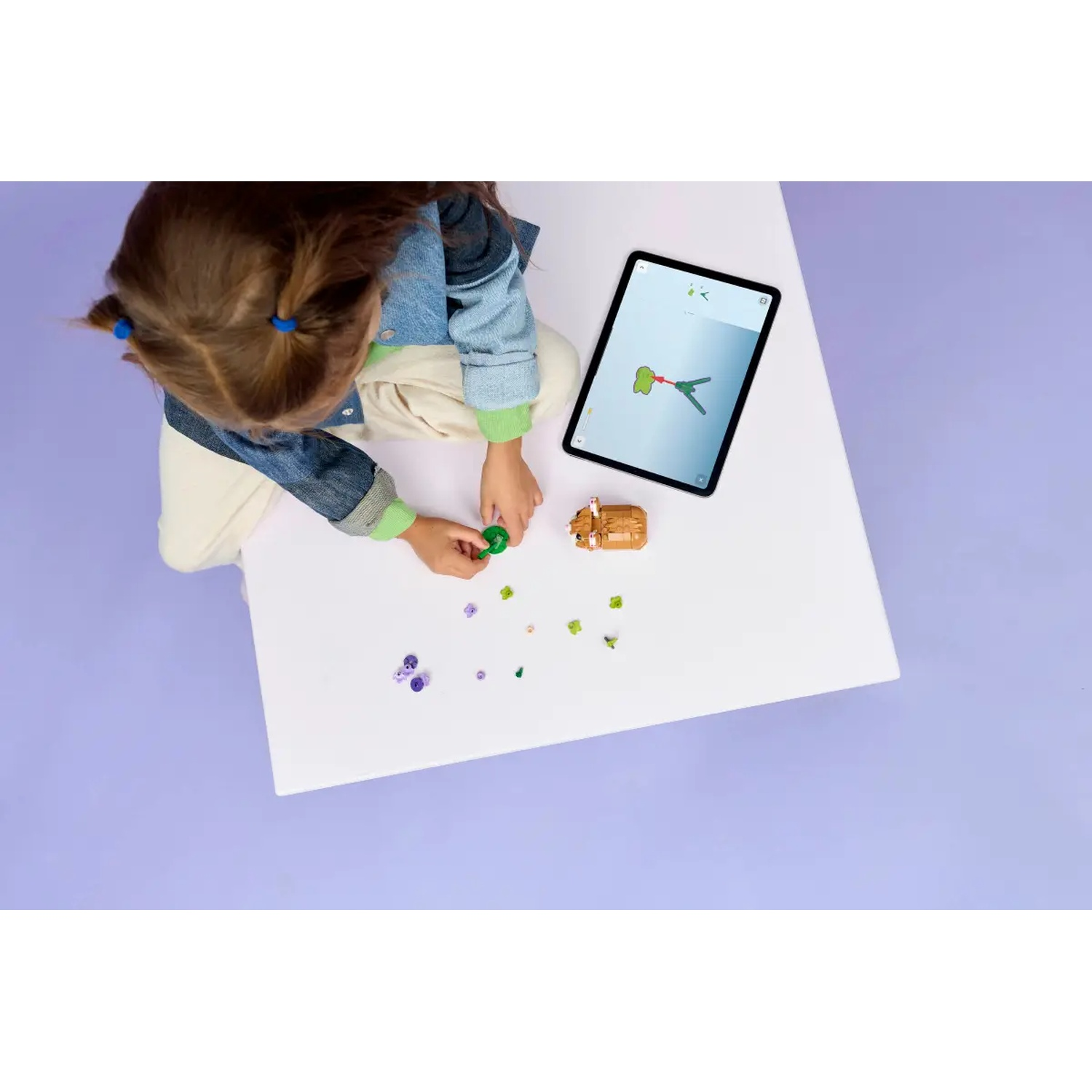 Een kind speelt met speelgoedstukken op een witte tafel. Een tablet met een diagram is in de buurt. De achtergrond is paars.