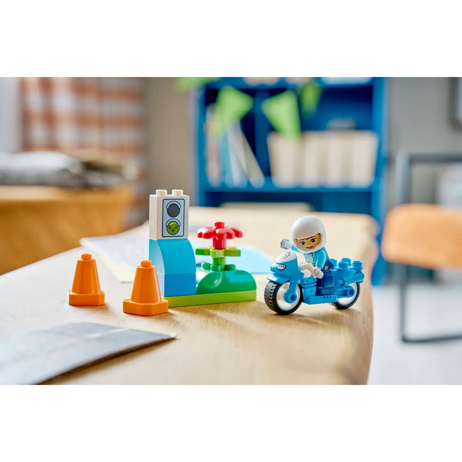 Un ensemble Lego avec un feu de signalisation, des cônes et une moto avec un pilote. L'arrière-plan comprend des étagères et une table en bois.