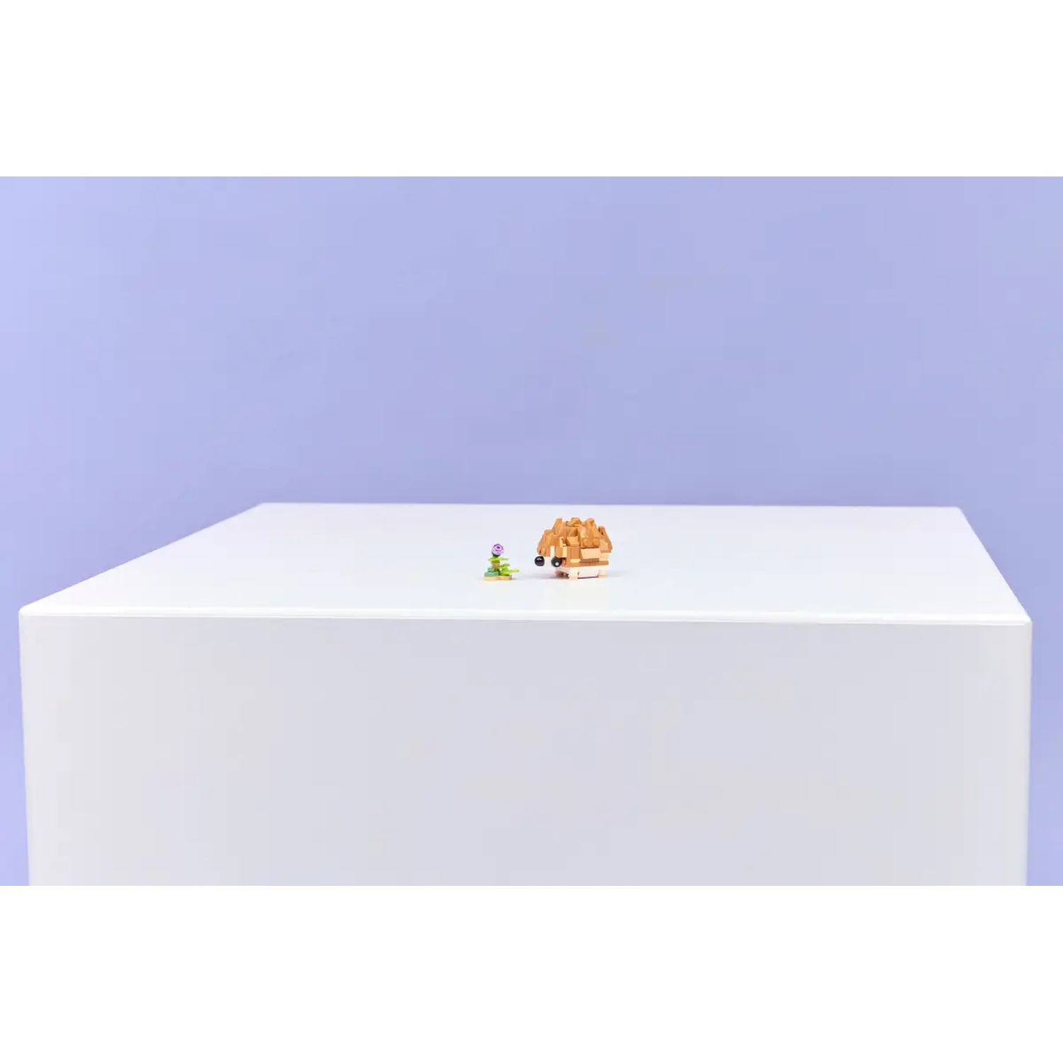 Een witte kubus met een klein speelgoedegel en een bloem. De achtergrond is lichtpaars.