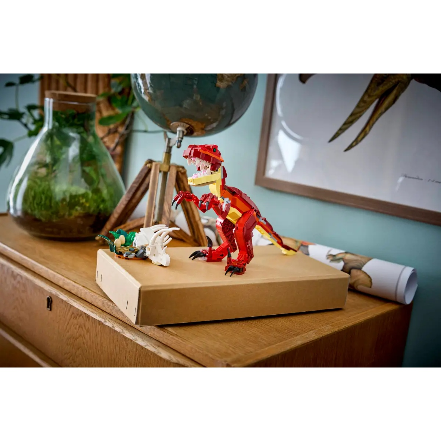 Een rode Lego-dino staat op een bruine doos met een witte botstructuur en een groene dino. Een wereldbol en een terrarium staan op de achtergrond.