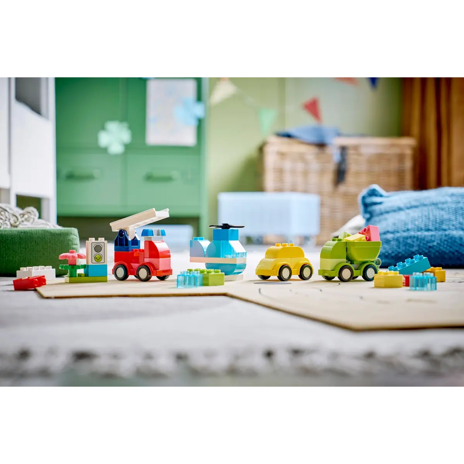 Des véhicules et des blocs de jouets colorés disposés sur un sol. Un camion de pompiers, un hélicoptère, une voiture et un tombereau sont visibles.