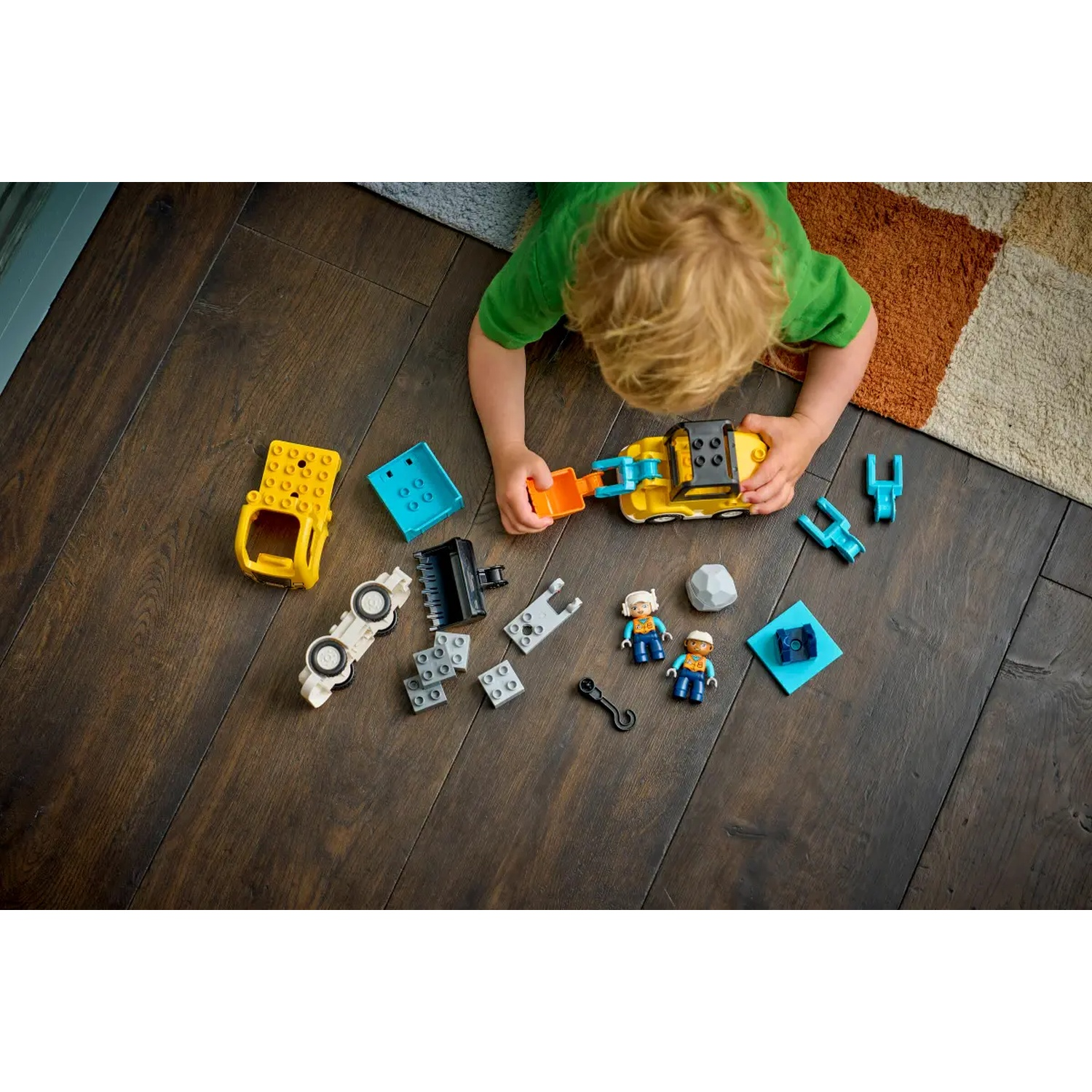 Un enfant joue avec des véhicules et des figurines de construction jouets sur un plancher en bois. Diverses pièces sont éparpillées.