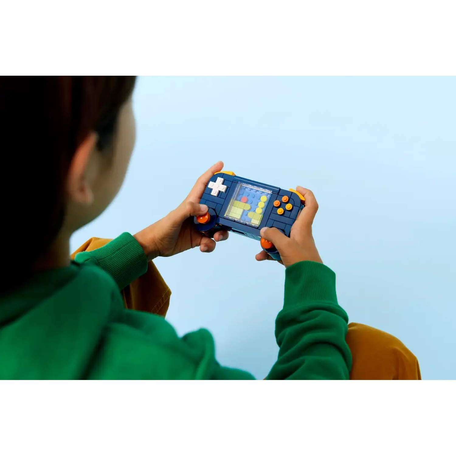 A child is holding a blue and orange toy game console, playing a game. The background is a light blue color.